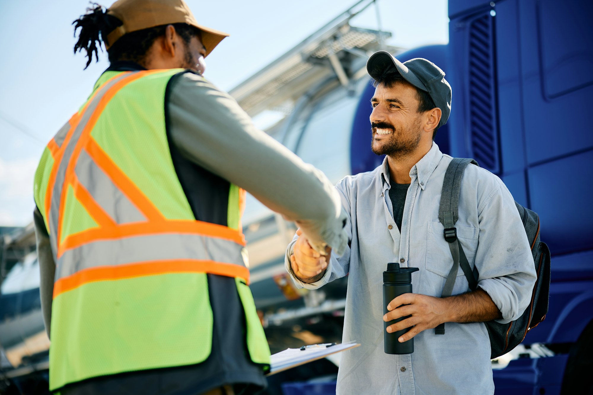 Happy truck driver greeting freight transportation manager on a parking lot.